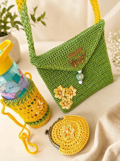 A crocheted green shoulder bag with a flap closure, decorated with yellow flowers and a butterfly embellishment, shown alongside a matching yellow crocheted bottle sleeve holding a water bottle and a small yellow coin purse on a neutral fabric surface.